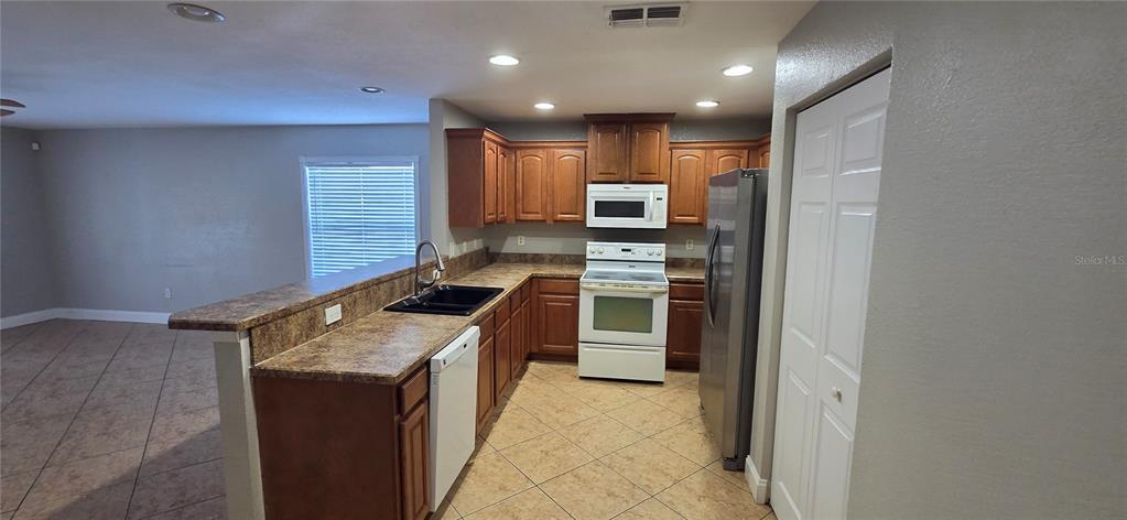 A kitchen with wood cabinets, laminate countertops, a white appliance suite, and tile flooring — 6807 E NORTH BAY STREET, TAMPA, FL