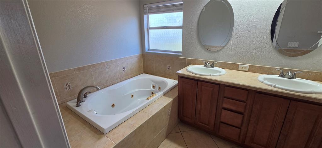 A bathroom features a jetted tub, double vanity with oval sinks, and beige tile finishes — 6807 E NORTH BAY STREET, TAMPA, FL