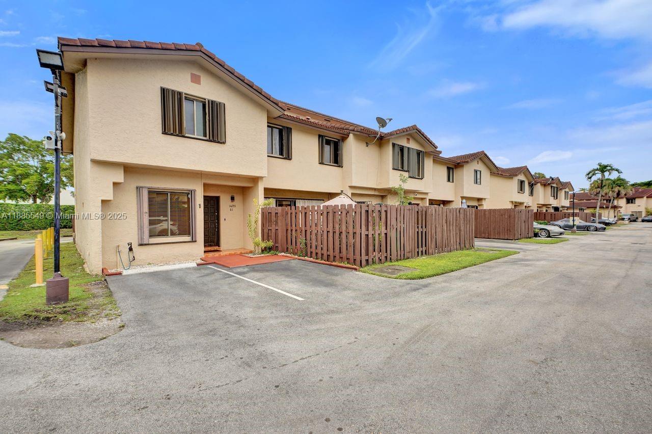 A two-story townhouse with a tan stucco exterior, a wooden privacy fence, and a parking space — 14201 SW 57th Ln, Miami FL 33183, MIAMI, FL