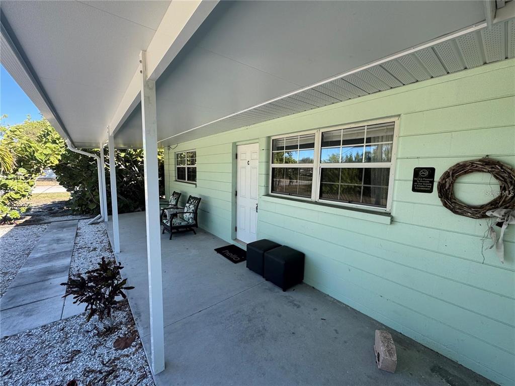 A light green house exterior features a covered porch with chairs and a white door — 104 BASE AVENUE W UNIT C, VENICE, FL