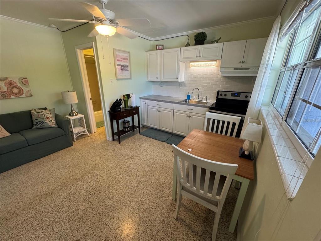 A small kitchen and living area features white cabinets, a dining table, and carpeted floors — 104 BASE AVENUE W UNIT C, VENICE, FL