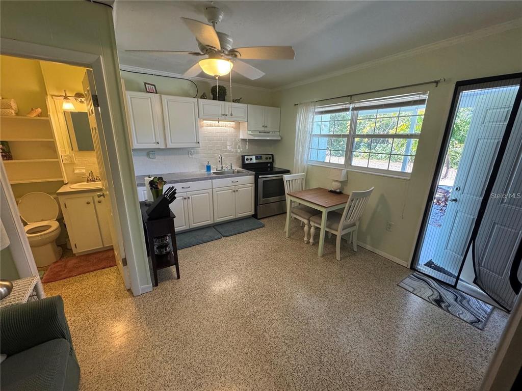 A kitchen with white cabinets, a small dining table, and a bathroom doorway — 104 BASE AVENUE W UNIT C, VENICE, FL