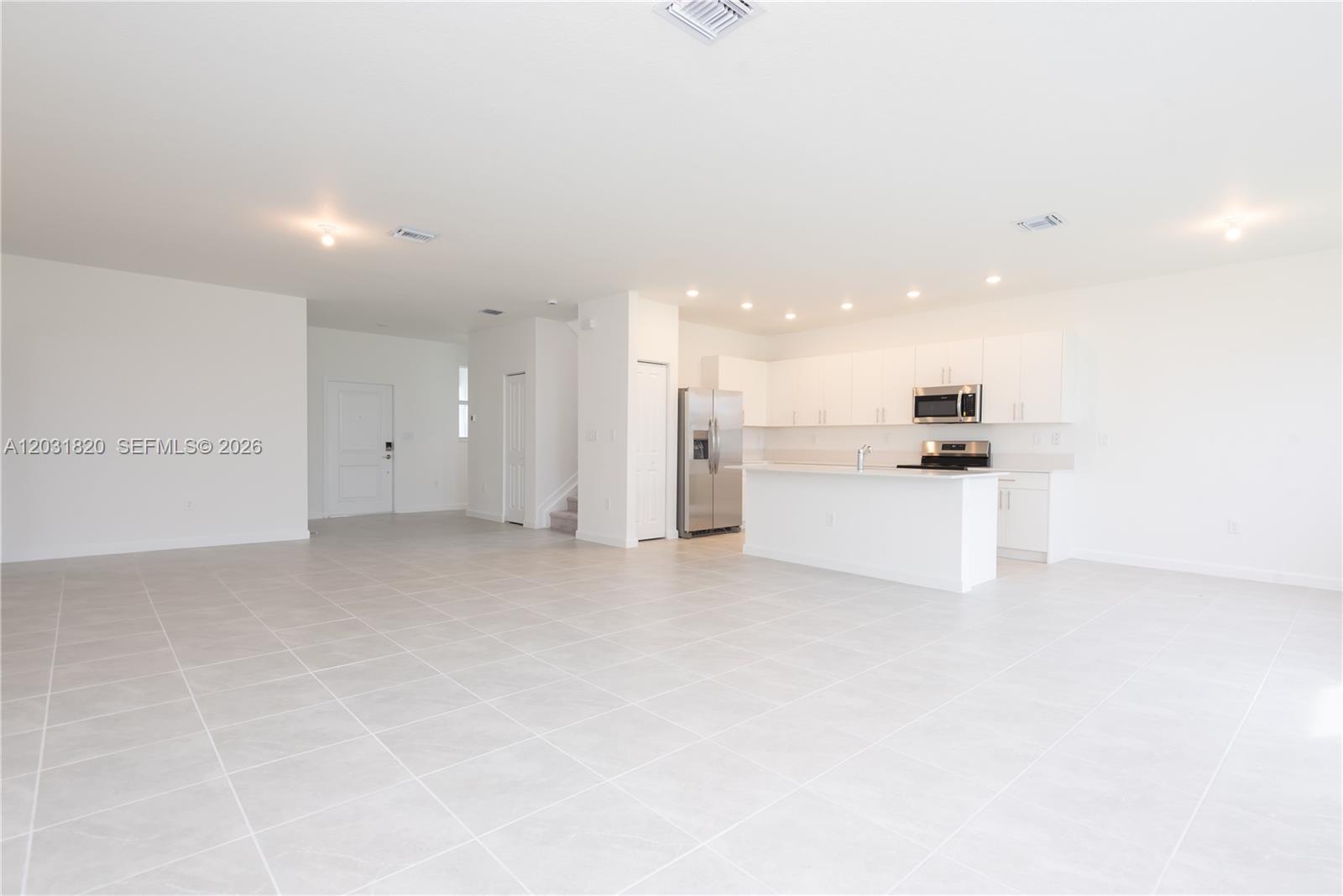 An open-concept kitchen and living area features white cabinetry, stainless steel appliances, and tile flooring — 2636 SE 8th Ct, Homestead FL 33035, HOMESTEAD, FL