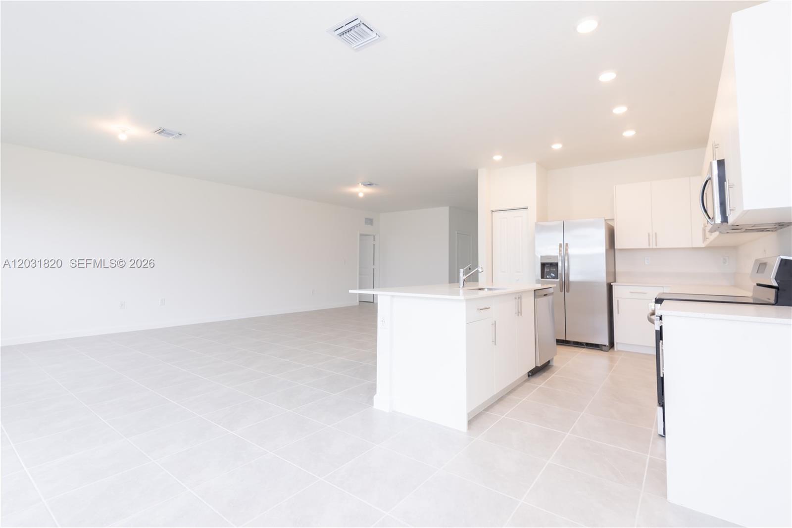 A modern kitchen with white cabinets and stainless steel appliances opens into a large room — 2636 SE 8th Ct, Homestead FL 33035, HOMESTEAD, FL