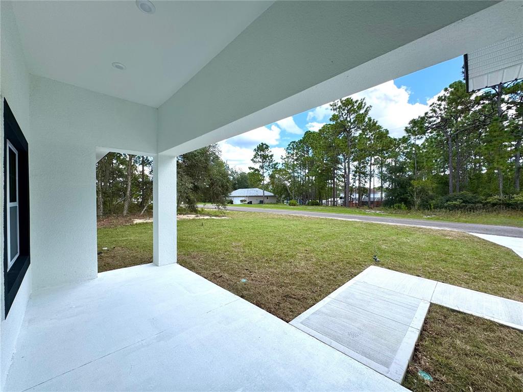 A covered concrete porch overlooks a grassy yard with trees and a neighboring house — 2077 W LINDEN DRIVE, CITRUS SPRINGS, FL
