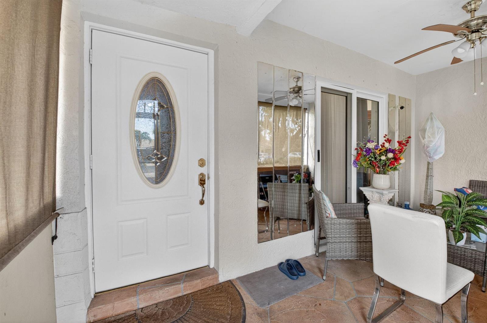 A covered patio features a white front door, mirrored wall panels, and outdoor furniture — 14232 Campanelli Drive, Delray Beach FL 33484, DELRAY BEACH, FL