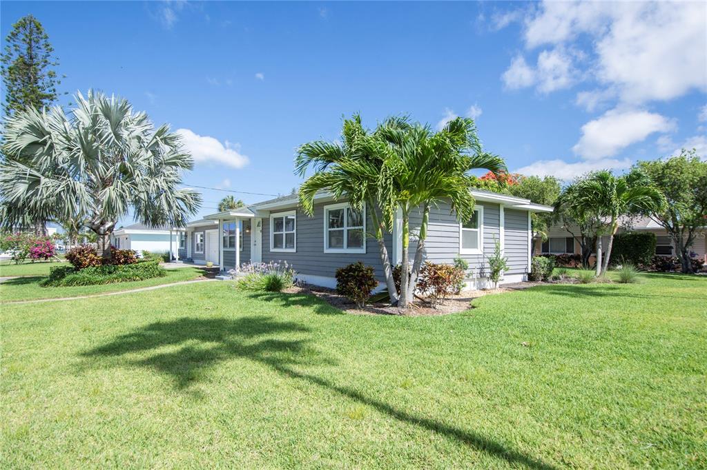A gray, single-story house with horizontal siding and palm trees sits on a grassy lawn — 3200 W DE BAZAN AVENUE, ST PETE BEACH, FL