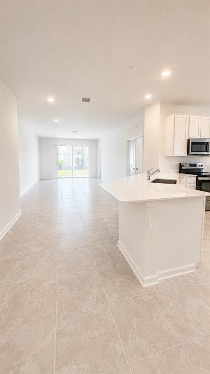 A bright kitchen with white cabinets and a quartz island opens to a tiled living area — 506 HATTERAS ROAD, DAVENPORT, FL