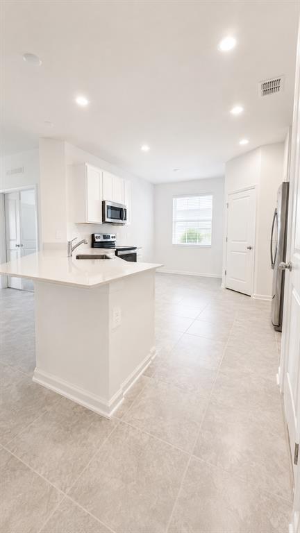 A bright kitchen features white cabinets, stainless steel appliances, a center island, and tile flooring — 506 HATTERAS ROAD, DAVENPORT, FL