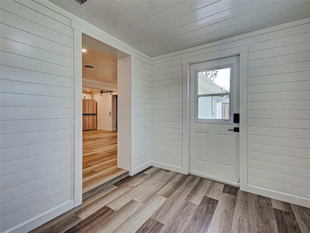 A room with white shiplap walls, wood-look flooring, and a door leading to the outside — 425 YALE STREET, ENGLEWOOD, FL