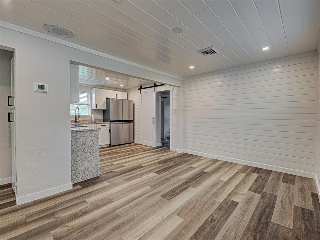 A room with wood-look flooring, shiplap walls, and a view into a kitchen with stainless appliances — 425 YALE STREET, ENGLEWOOD, FL