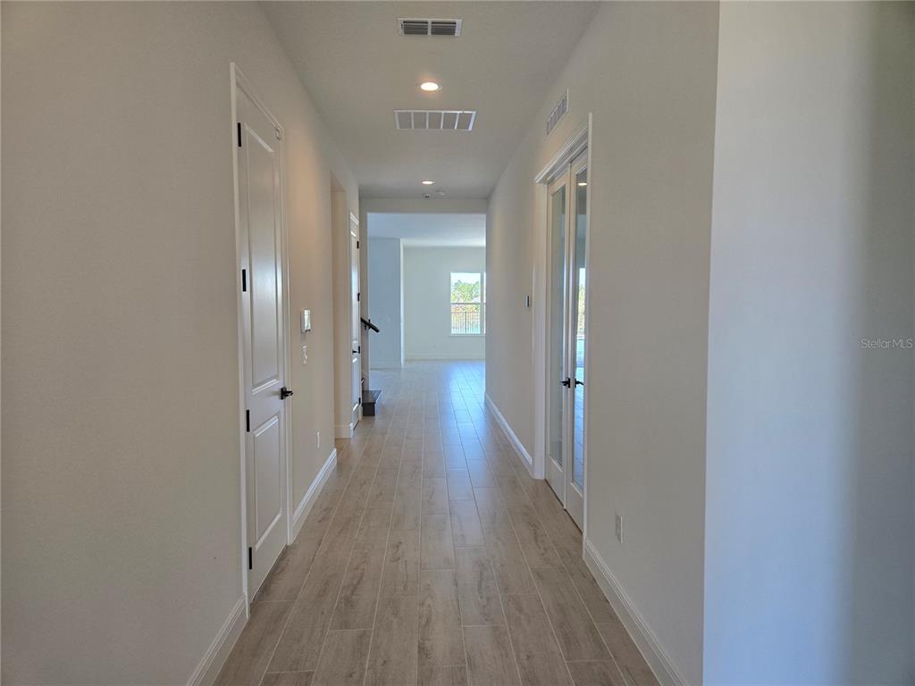 A long hallway with light wood-look tile flooring leads toward a bright, open living area — 13217 TOLLCROSS WAY, WINTER GARDEN, FL