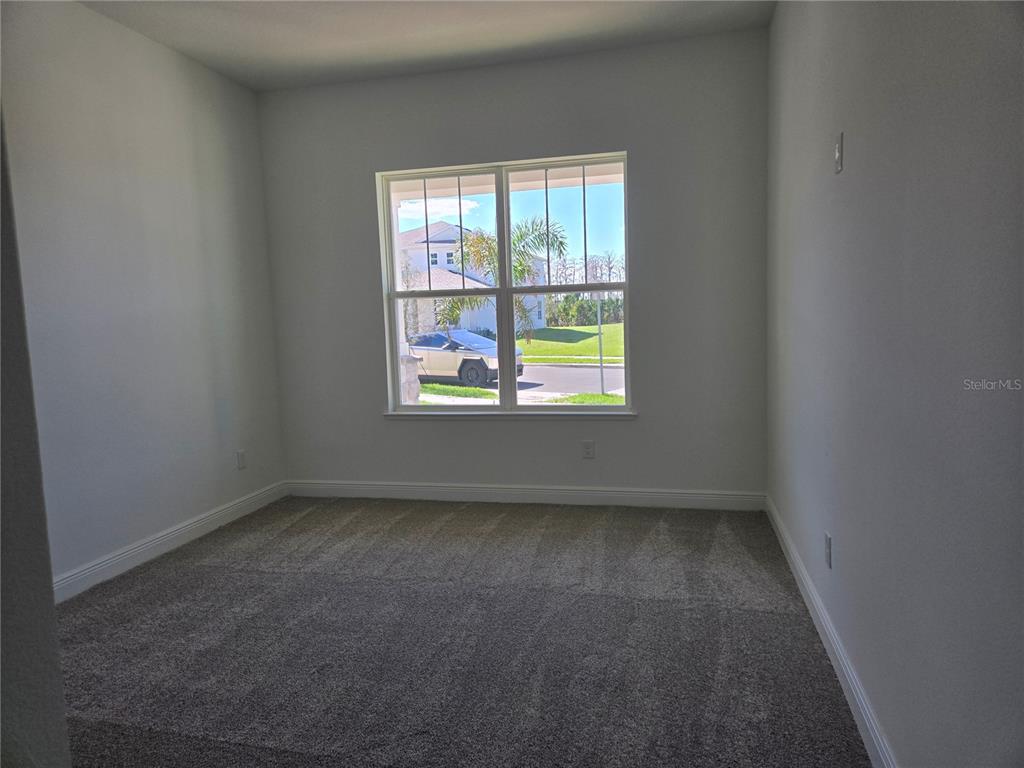 An empty bedroom features gray carpet, white walls, and a window overlooking a suburban street — 13217 TOLLCROSS WAY, WINTER GARDEN, FL