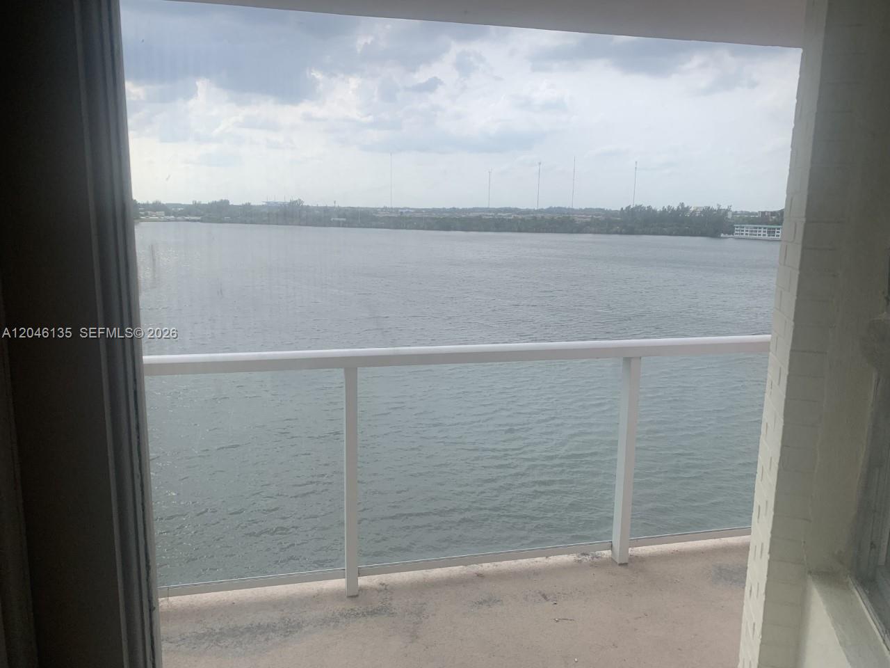 A balcony with a white railing overlooks a large body of water under a cloudy sky — MIAMI, FL
