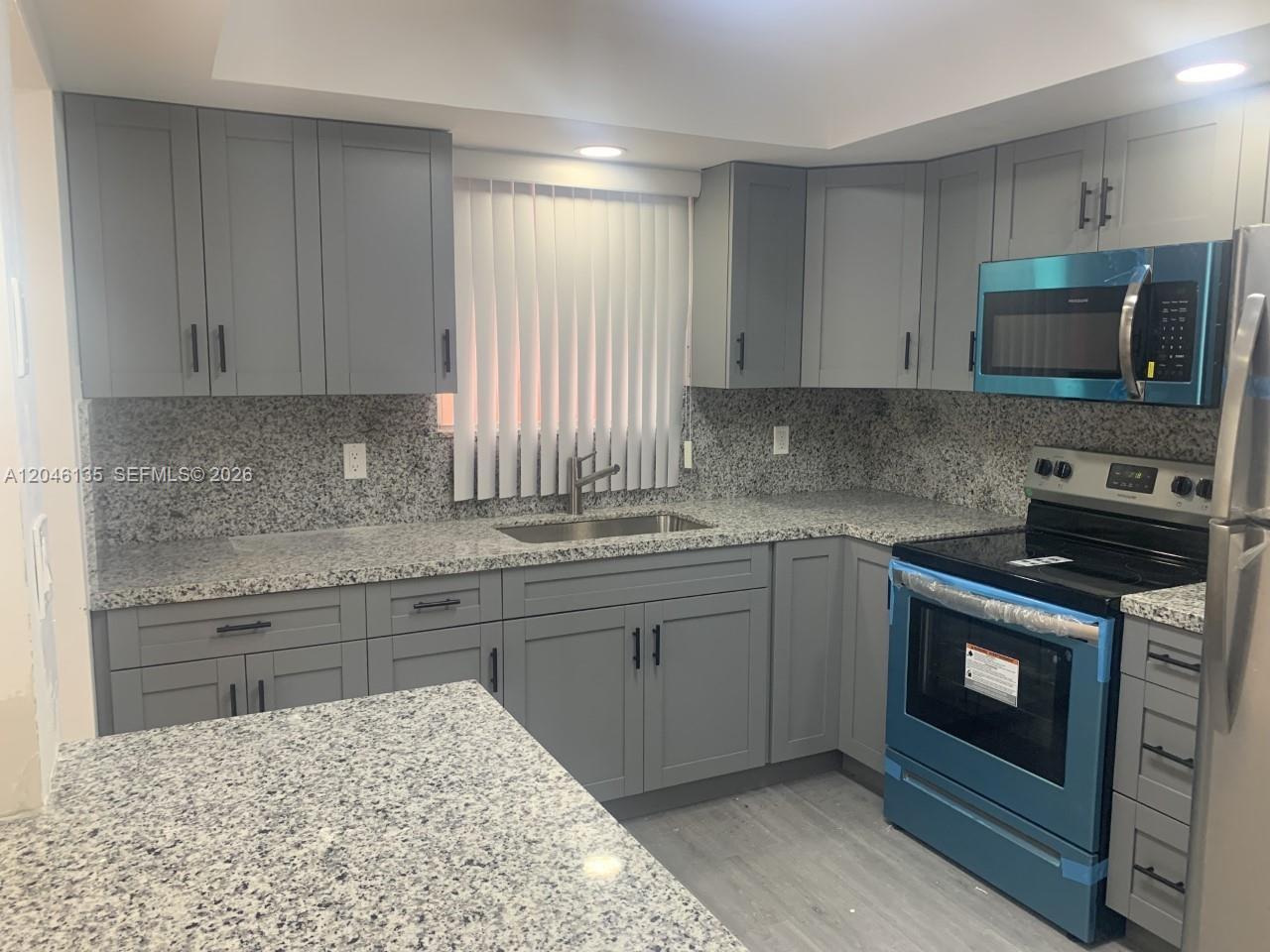 A kitchen features gray shaker cabinets, granite countertops, and stainless steel appliances — MIAMI, FL