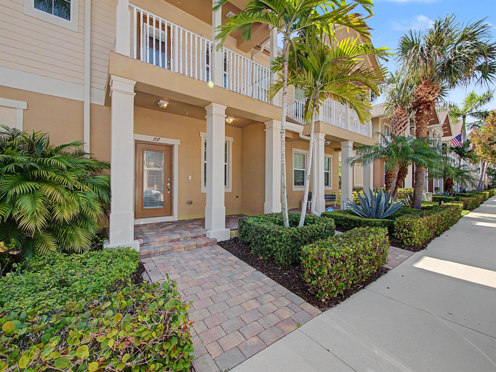 A tan multi-story building features a brick walkway leading to a front door numbered 107 — 118 Black Ironwood Road # 107, Jupiter FL 33458, JUPITER, FL