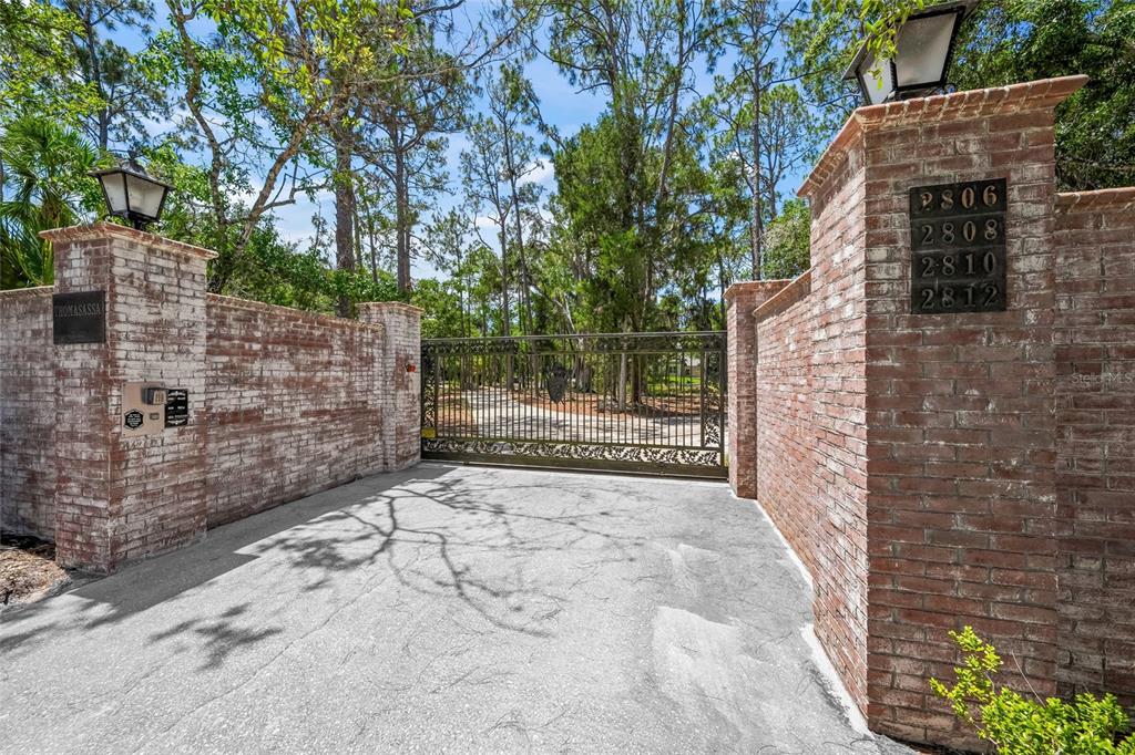 A gated entrance with brick pillars and a metal driveway gate surrounded by trees — 2810 SARASOTA GOLF CLUB BOULEVARD, SARASOTA, FL