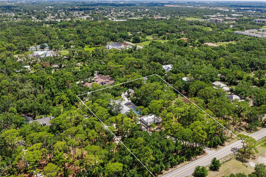 An aerial view shows a house with a pool surrounded by trees near a road — 2810 SARASOTA GOLF CLUB BOULEVARD, SARASOTA, FL