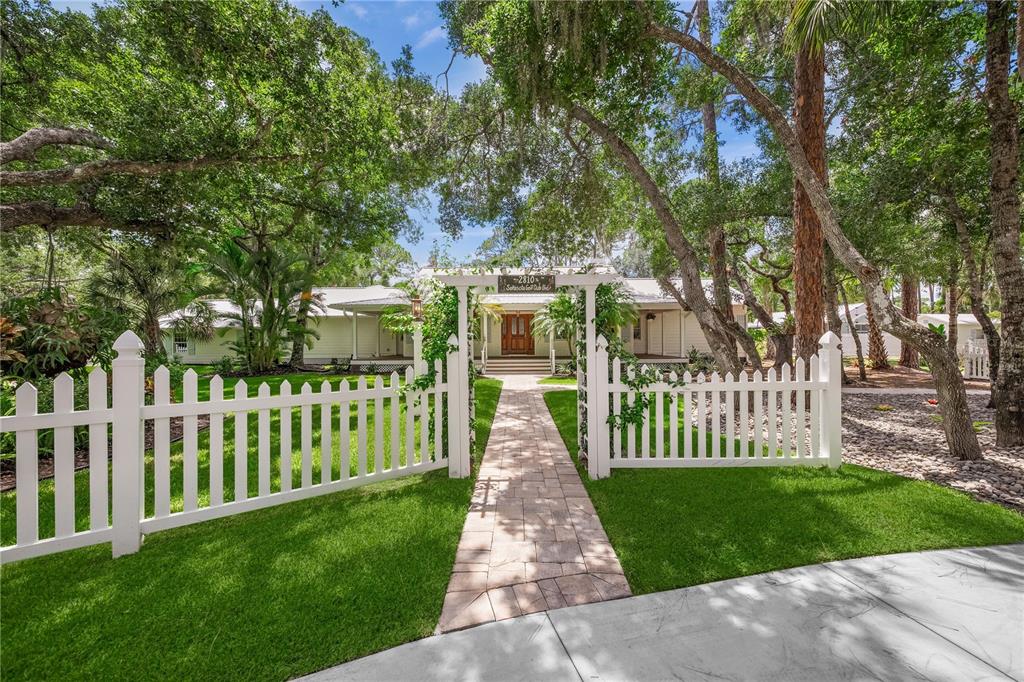 A white picket fence surrounds a front yard with a stone walkway leading to a house — 2810 SARASOTA GOLF CLUB BOULEVARD, SARASOTA, FL