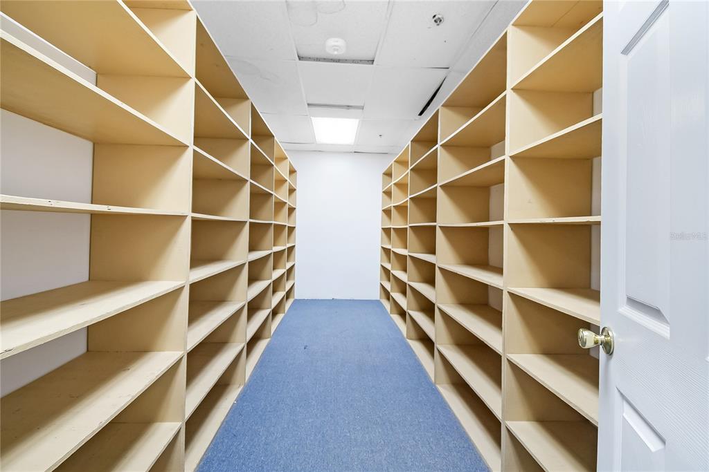 A narrow storage room features floor-to-ceiling wooden shelving units on both sides and blue carpeting — 233 E BAY STREET UNIT 1016, JACKSONVILLE, FL