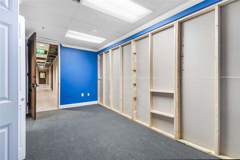 An office room features a blue accent wall, gray carpet, and an unfinished wood-framed wall — 233 E BAY STREET UNIT 1016, JACKSONVILLE, FL