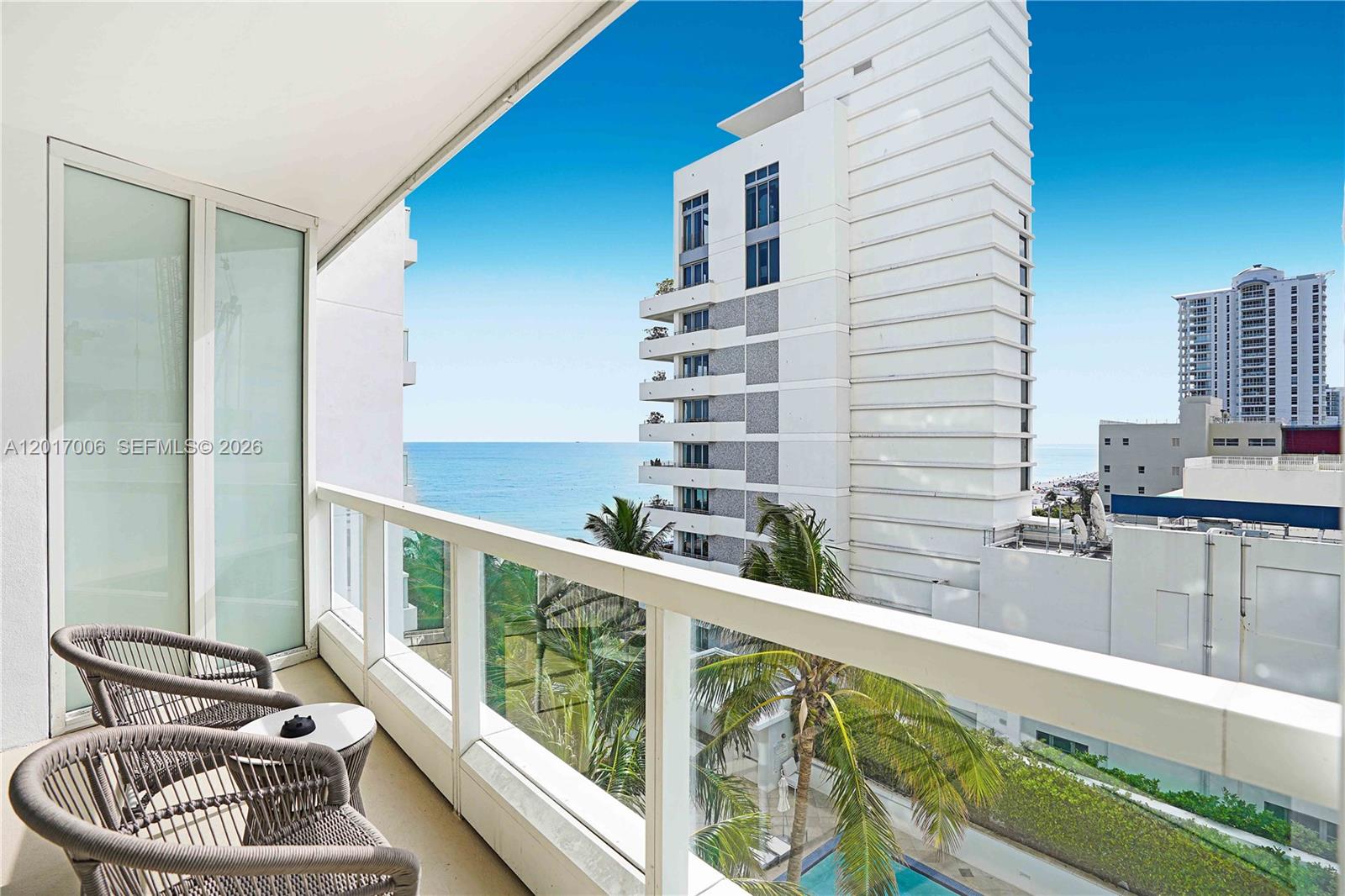 A balcony with two chairs overlooks a swimming pool, palm trees, and the ocean — 4391 Collins Ave # 916, Miami Beach FL 33140, MIAMI BEACH, FL
