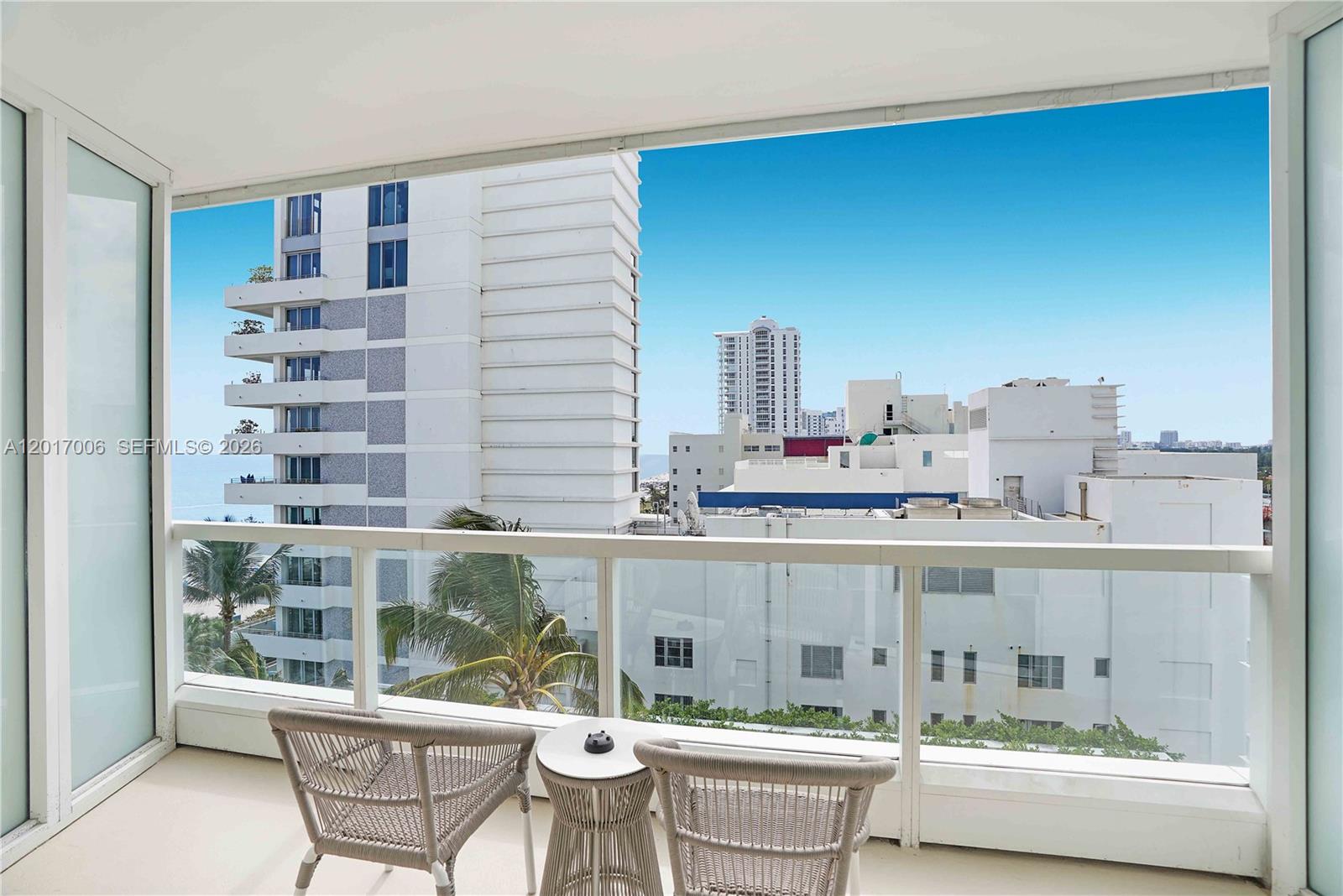 A balcony with two chairs and a small table overlooks a city skyline and ocean — 4391 Collins Ave # 916, Miami Beach FL 33140, MIAMI BEACH, FL