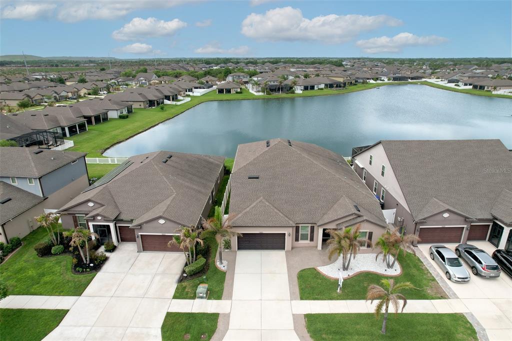 An aerial view shows three suburban houses with driveways and garages facing a large lake — 13821 TONYA ANNE DRIVE, RIVERVIEW, FL