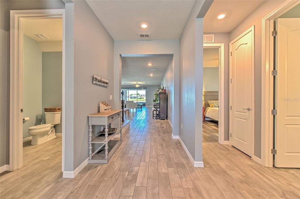 A hallway with light wood-look tile floors leads toward a living area with a view — 13821 TONYA ANNE DRIVE, RIVERVIEW, FL