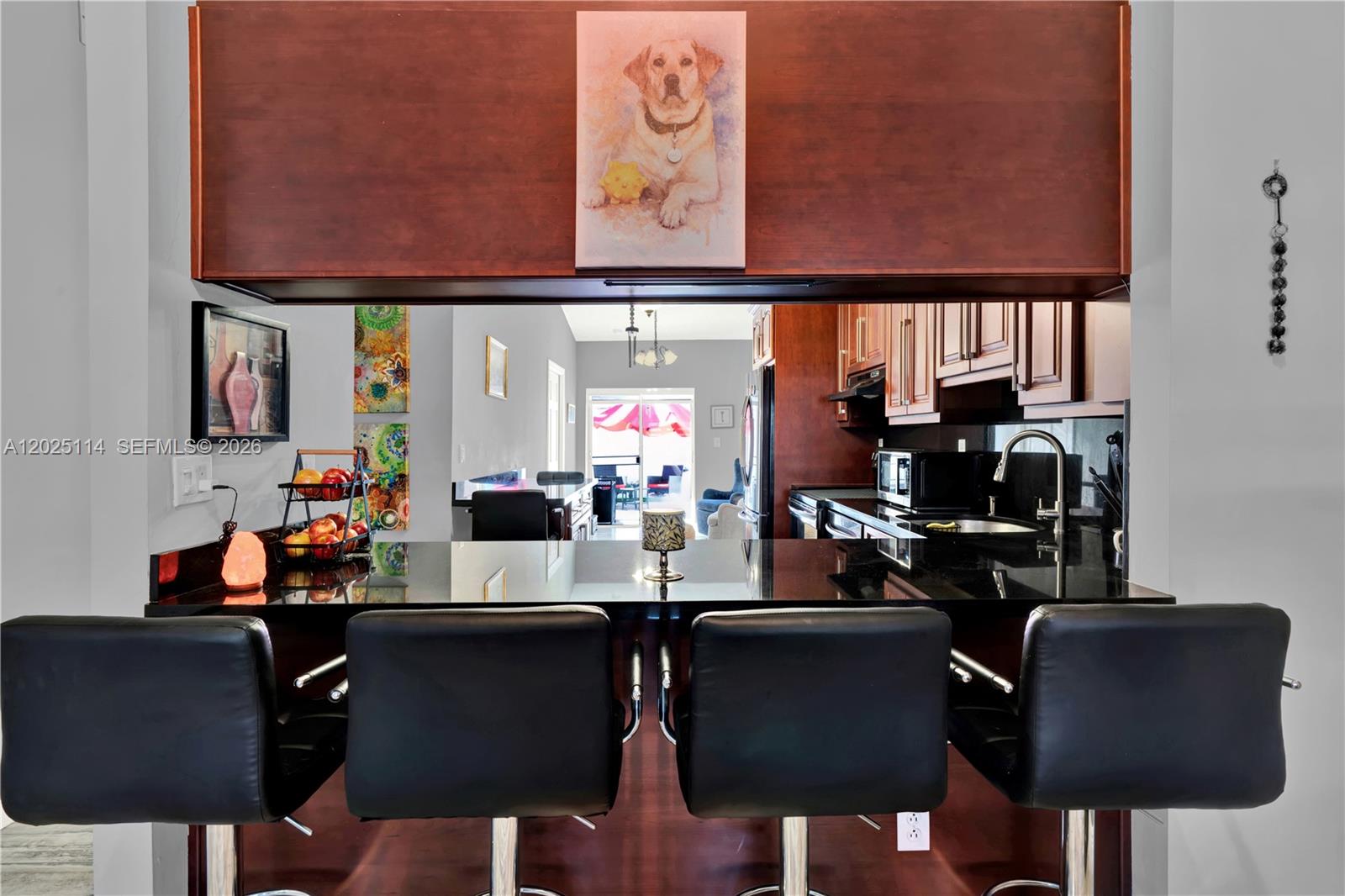 A kitchen features a black granite breakfast bar with four black stools and wood cabinetry — 7462 W 29th Way, Hialeah FL 33018, HIALEAH, FL