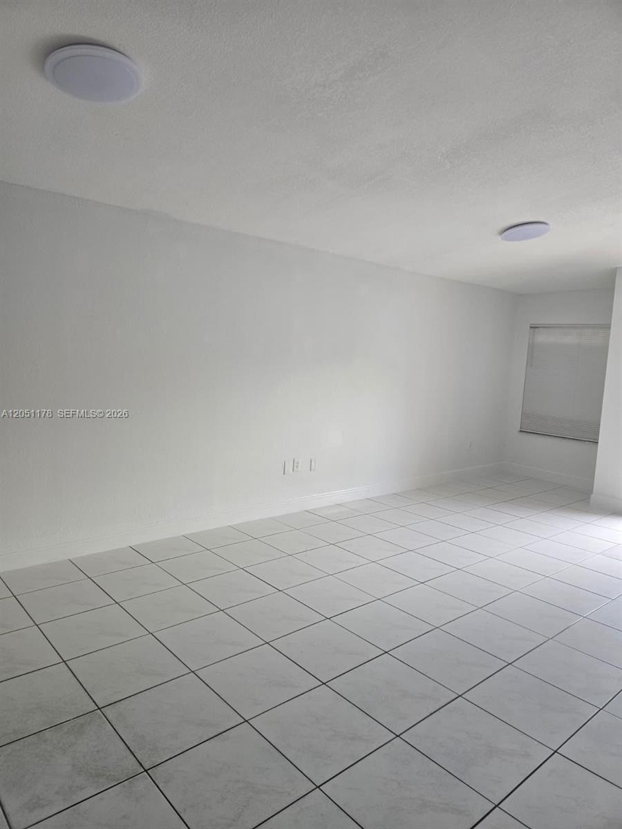 An empty room features white walls, white tiled floors, and two flush-mount ceiling lights — 9069 NW 121st Ter # 81, Hialeah Gardens FL 33018, HIALEAH GARDENS, FL