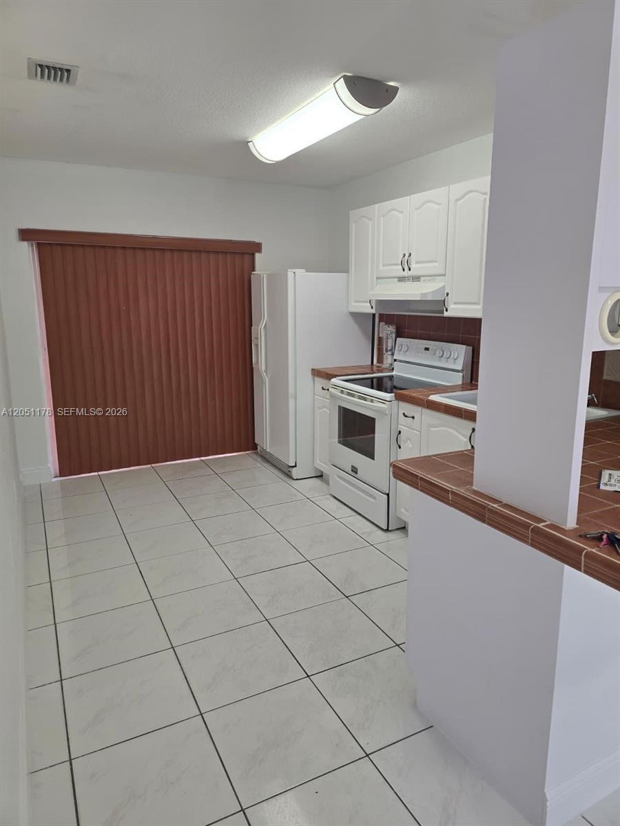 A kitchen features white cabinets, white appliances, and light-colored tile flooring — 9069 NW 121st Ter # 81, Hialeah Gardens FL 33018, HIALEAH GARDENS, FL