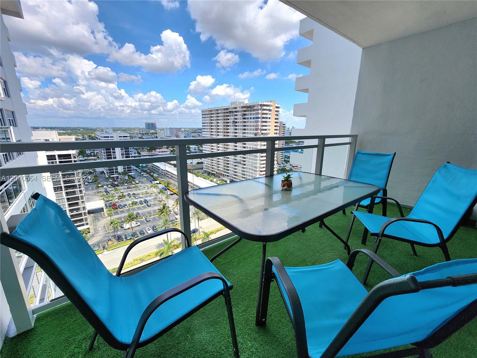 A balcony with artificial turf, a glass-top table, and four blue chairs overlooks a city — 2030 S Ocean Dr # 1803, Hallandale Beach FL 33009, HALLANDALE BEACH, FL