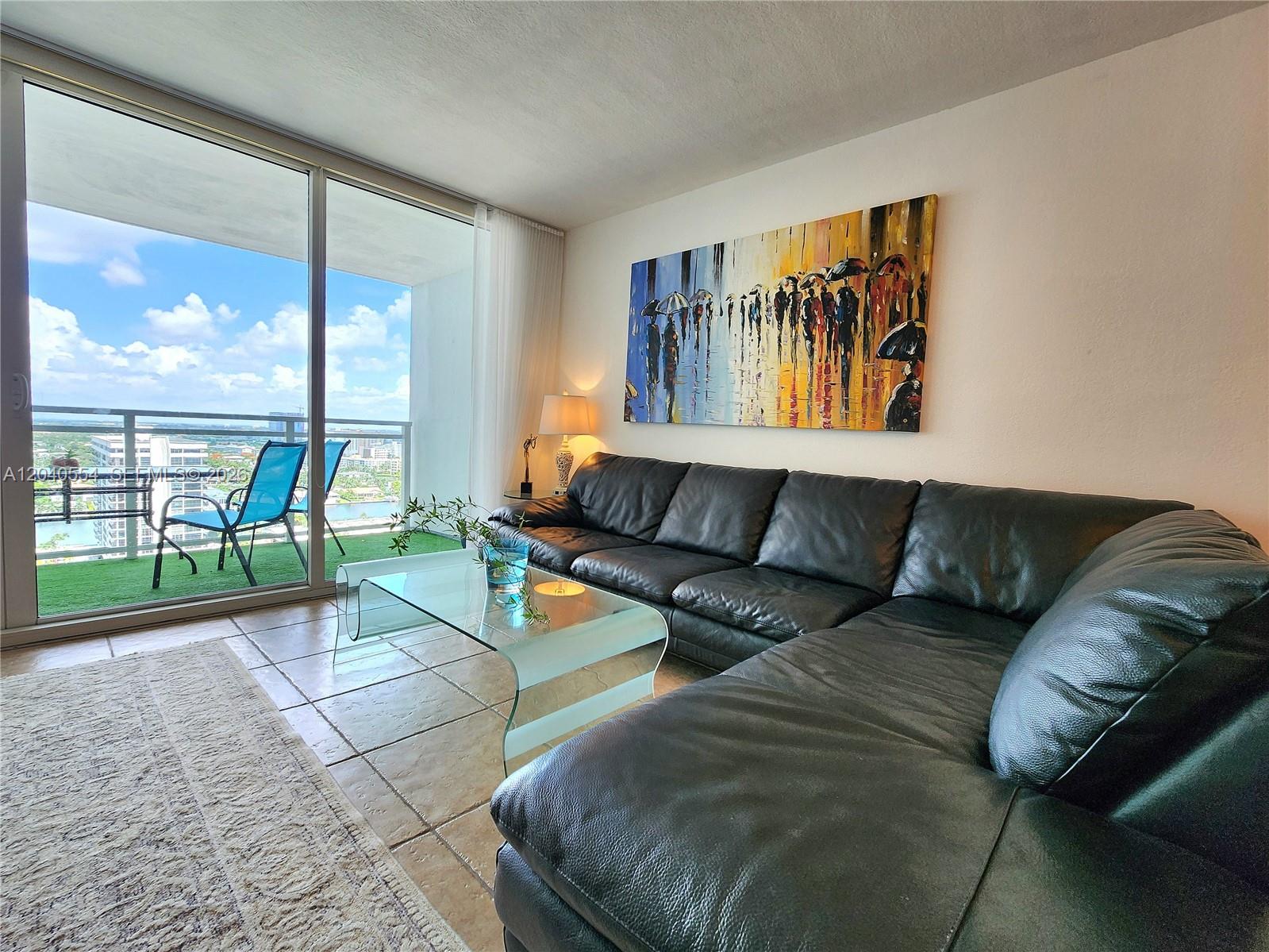 A living room features a black leather sectional, glass coffee table, and a balcony view — 2030 S Ocean Dr # 1803, Hallandale Beach FL 33009, HALLANDALE BEACH, FL