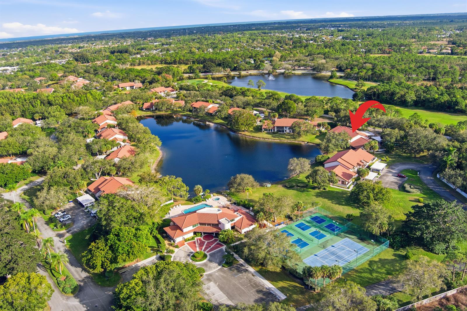 An aerial view shows a residential complex with a lake, tennis courts, and swimming pool — 6100 SE Martinique Drive # 201, Stuart FL 34997, STUART, FL