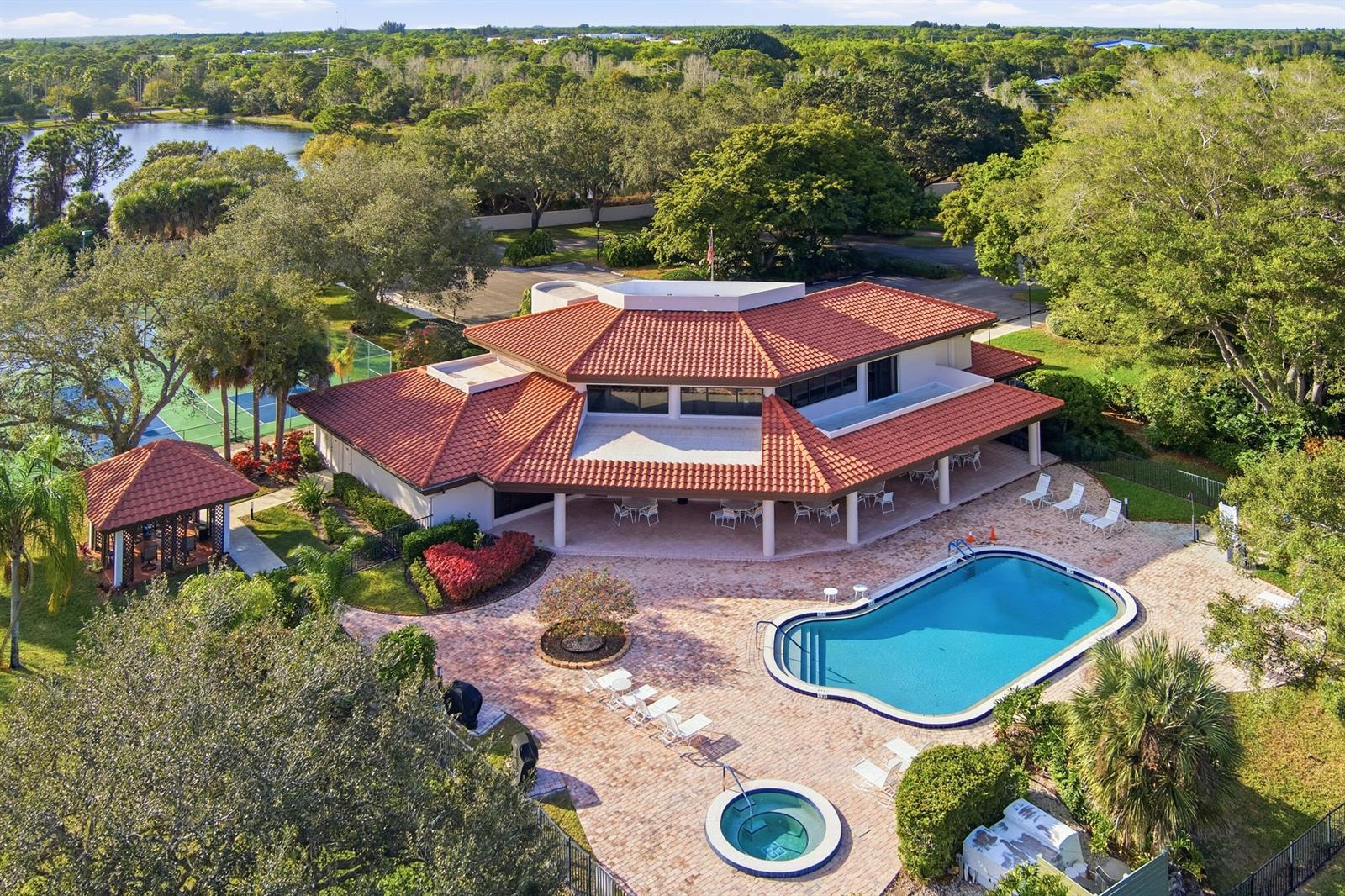 An aerial view shows a clubhouse with a red tile roof, pool, hot tub, and tennis courts — 6100 SE Martinique Drive # 201, Stuart FL 34997, STUART, FL