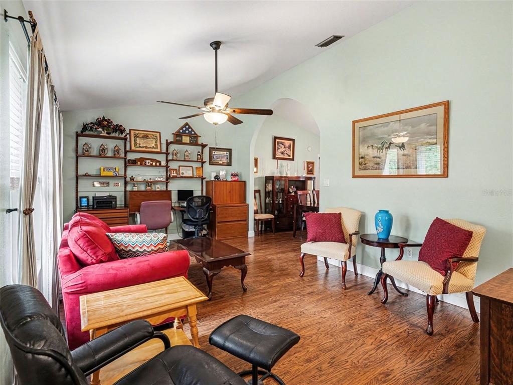 A living room features a red sofa, two accent chairs, wood flooring, and wall shelving — 507 RAMBLEWOOD STREET, PORT CHARLOTTE, FL