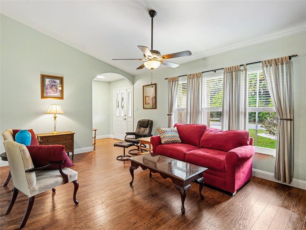 A living room features hardwood floors, a red sofa, a ceiling fan, and large windows — 507 RAMBLEWOOD STREET, PORT CHARLOTTE, FL