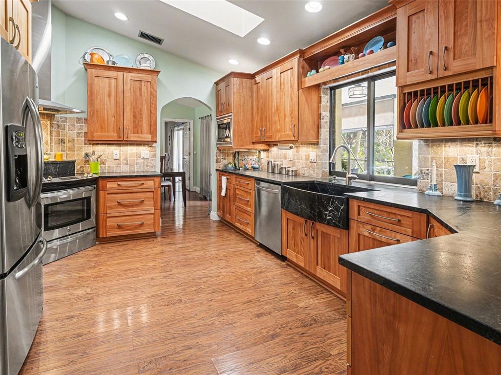 A kitchen with wood cabinets, dark countertops, stainless steel appliances, and a black farmhouse sink — 507 RAMBLEWOOD STREET, PORT CHARLOTTE, FL