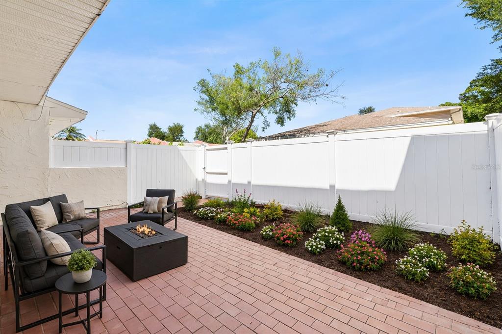 A patio with brick pavers, a fire pit, outdoor seating, and a white vinyl fence — 7256 MOFFATT LANE N, PINELLAS PARK, FL