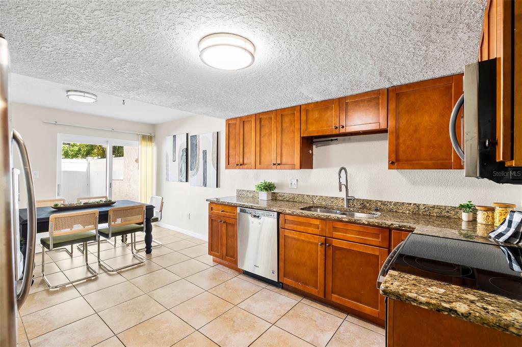 A kitchen with wood cabinets, granite countertops, and stainless steel appliances next to a dining area — 7256 MOFFATT LANE N, PINELLAS PARK, FL