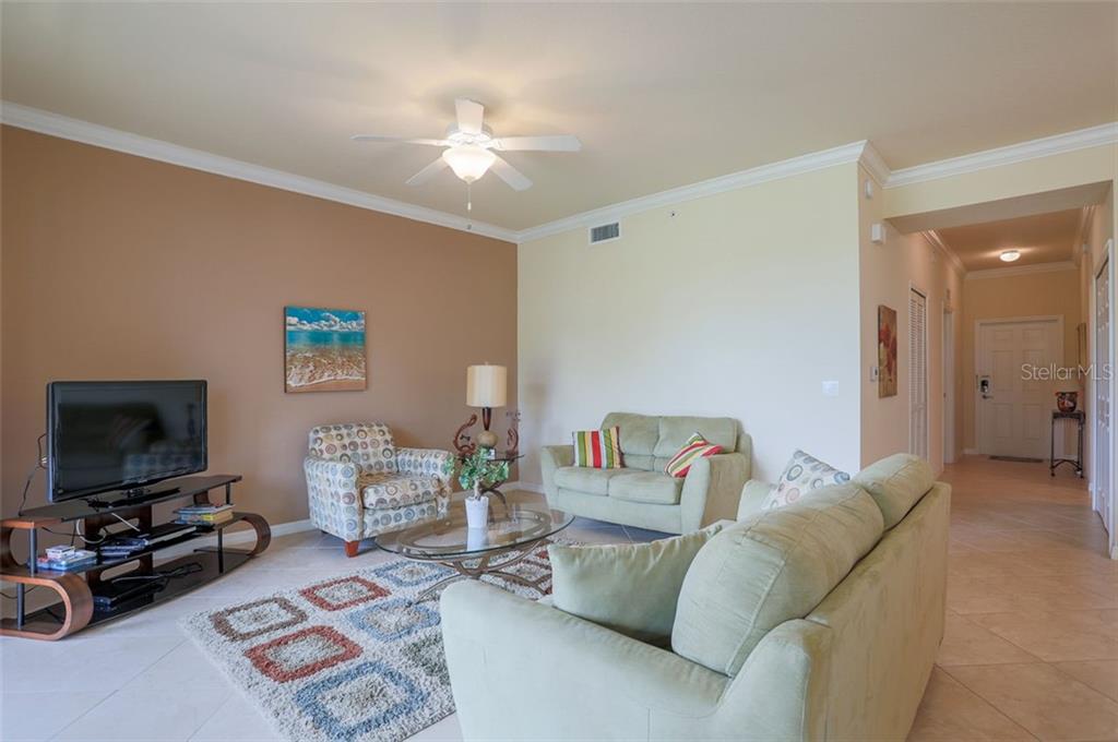 A living room features a television, a patterned armchair, two sofas, and a ceiling fan — 8105 GRAND ESTUARY TRAIL UNIT 106, BRADENTON, FL