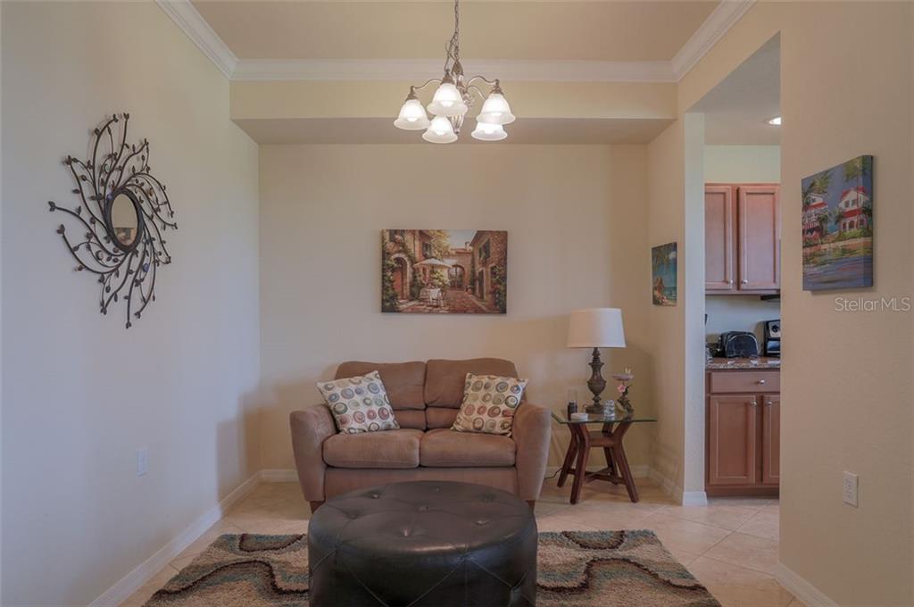 A living area features a tan loveseat, a round leather ottoman, and a chandelier — 8105 GRAND ESTUARY TRAIL UNIT 106, BRADENTON, FL