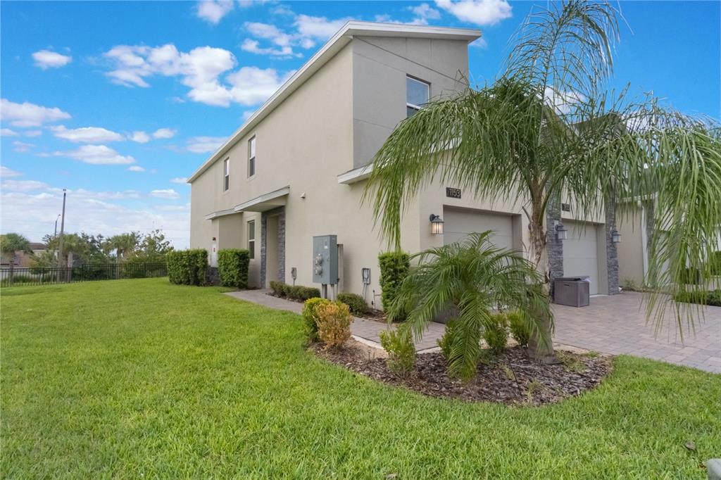A two-story townhouse with a beige stucco exterior, a paved driveway, and a palm tree — 1153 DROP LANE, DAVENPORT, FL