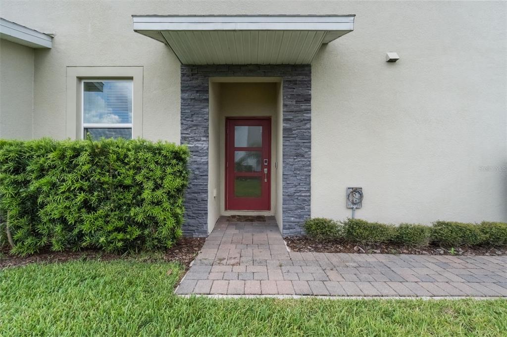 A red front door with glass panels is framed by stone veneer under a porch overhang — 1153 DROP LANE, DAVENPORT, FL