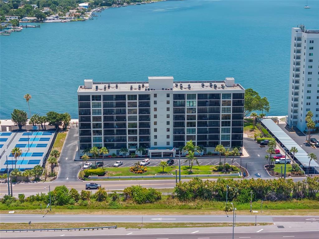 An aerial view shows a multi-story apartment building situated along a waterfront with parking — 7100 SUNSHINE SKYWAY LANE S UNIT 703, ST PETERSBURG, FL
