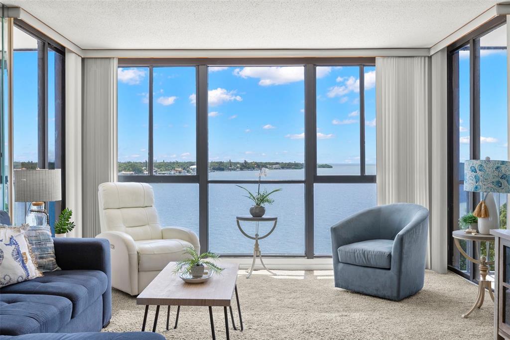 A living room with a blue sofa, white recliner, and large windows overlooking the water — 7100 SUNSHINE SKYWAY LANE S UNIT 703, ST PETERSBURG, FL