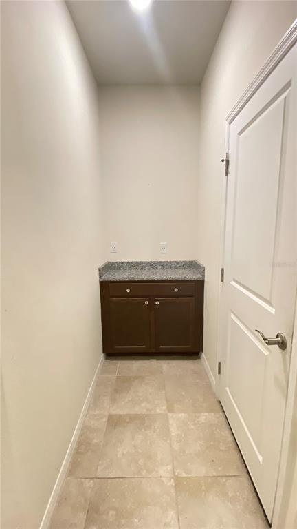A small laundry room features a dark wood cabinet with a granite countertop and tile flooring — 13515 PALMERA VISTA DRIVE, RIVERVIEW, FL