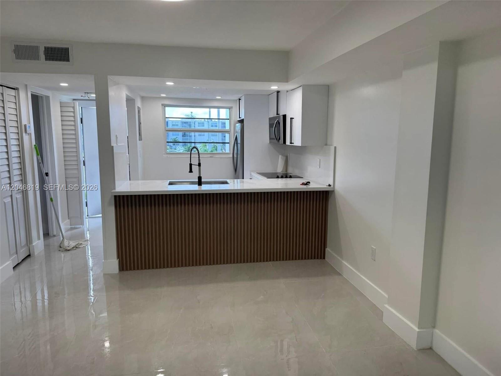 A kitchen features a wood-slatted peninsula, white cabinets, and light tile flooring — 14155 SW 87th St # E202, Miami FL 33183, MIAMI, FL