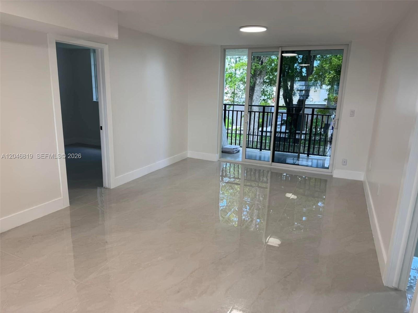 A bright room features glossy light-colored tile floors, white walls, and a sliding glass balcony door — 14155 SW 87th St # E202, Miami FL 33183, MIAMI, FL